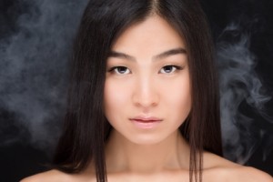 Asian woman beauty face close-up portrait. Beautiful attractive mixed race Chinese / Asian / Caucasian female model with perfect skin isolated over black background.