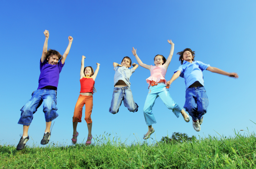 Group of five happy children jumping on meadow.