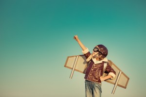 Kid pilot with toy jet pack against autumn sky background. Happy child playing outdoors