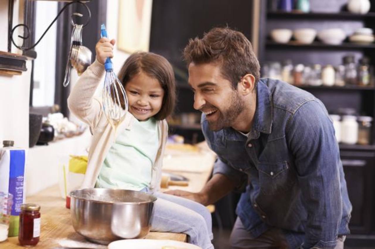 A cute little girl helping her dad make pancakes at home