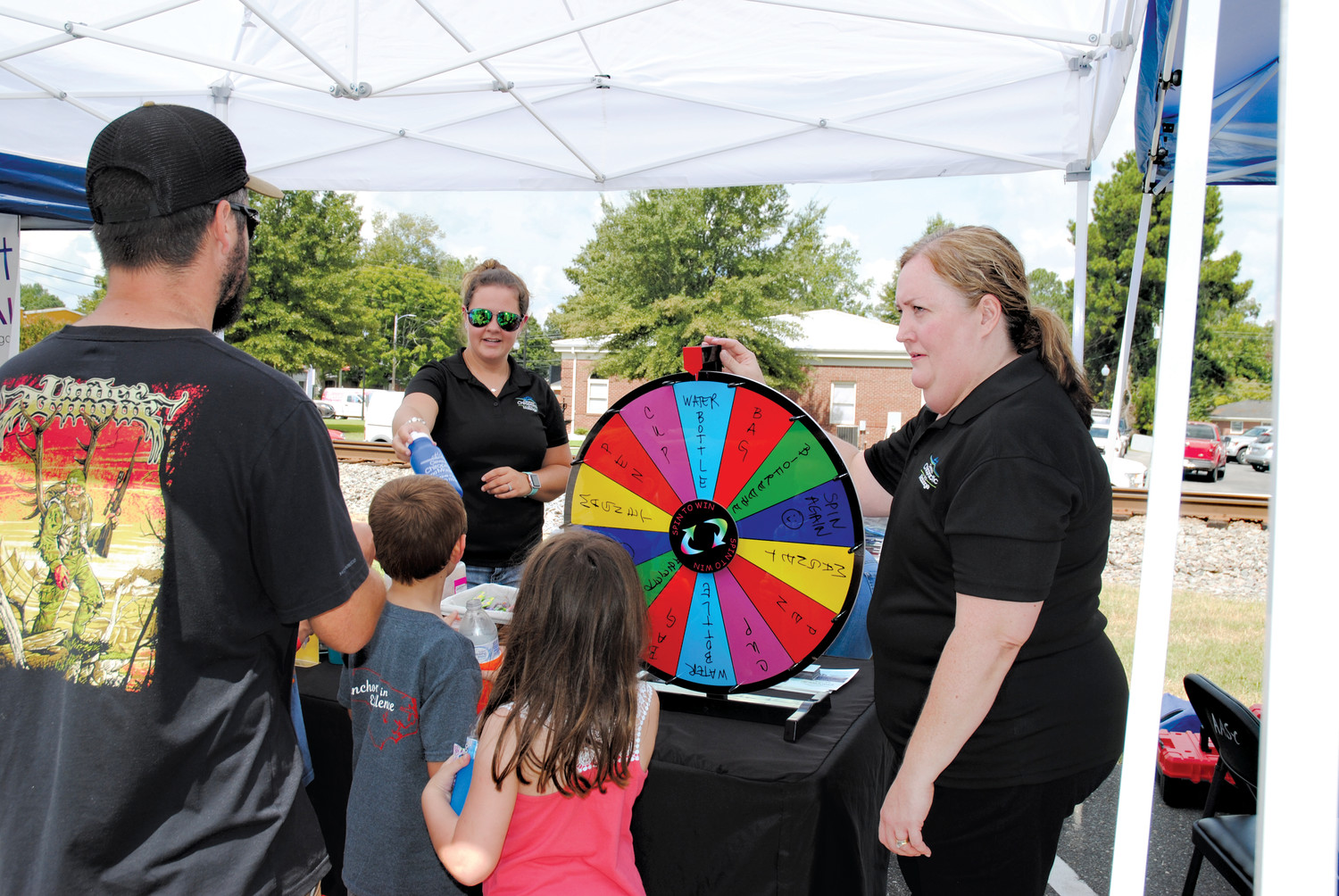 Businesses and organizations lined both sides of Railroad Avenue in Four Oaks Saturday for a Business Expo, part of the annual Acorn Festival. Here, Dr. Michelle Elliott, right, and Jamie Bell, left, of Cleveland Chiropractic and Massage watches as Jared Petterson of Four Oaks and his kids, Grayson, 6, and Reece, 9, spin the wheel for prizes.