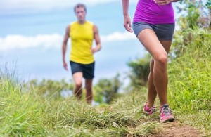 People running walking in nature on trail path. Group of runners hikers hiking in summer outdoors. Woman legs and man in the background. Fitness activity for a fit couple living a healthy lifestyle.